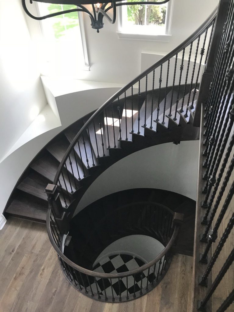 A dark wood spiral staircase with black iron spindles and a smooth handrail.