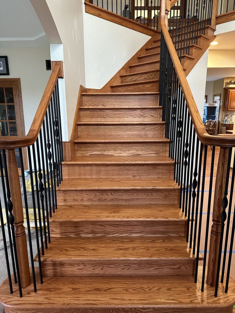 A beautiful finished oak staircase with black iron balusters and a smooth oak handrail.