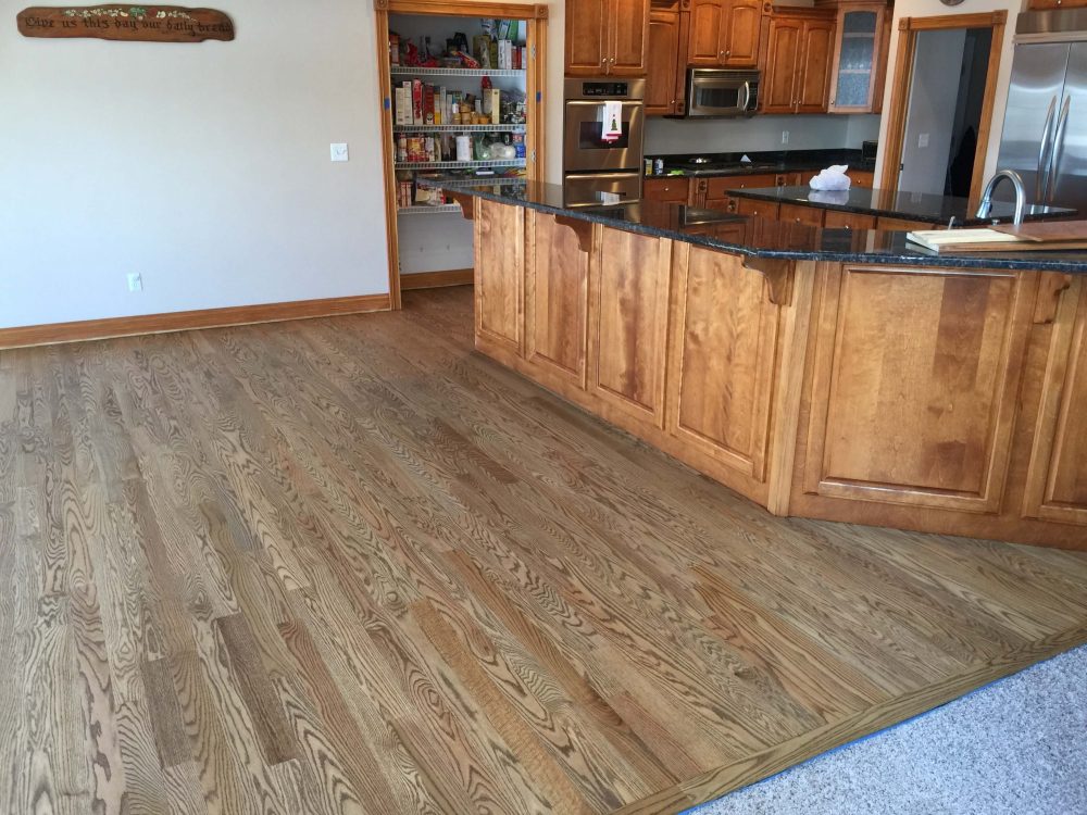 Hardwood floor finished with Rubio Monocoat in a kitchen with wood cabinets and dark countertops