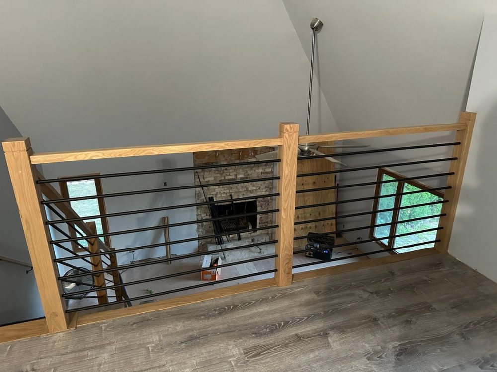 Finished loft guardrail: white oak rail and posts with horizontal iron spindles overlooking the living room in West Chicago, IL.