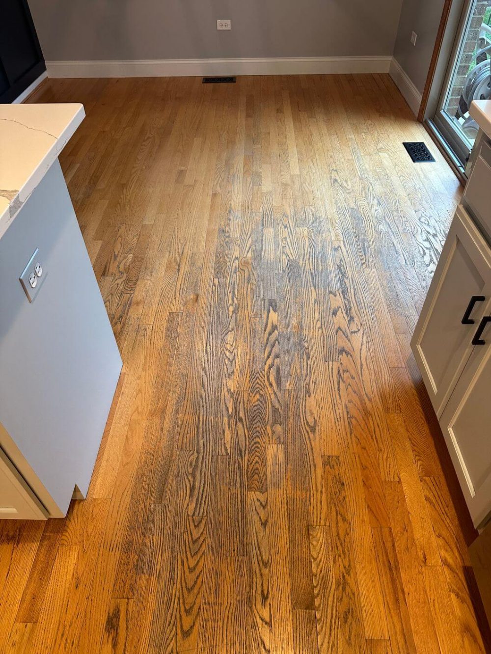 Before photo of old oak floors with faded finish and visible wear in the dining area