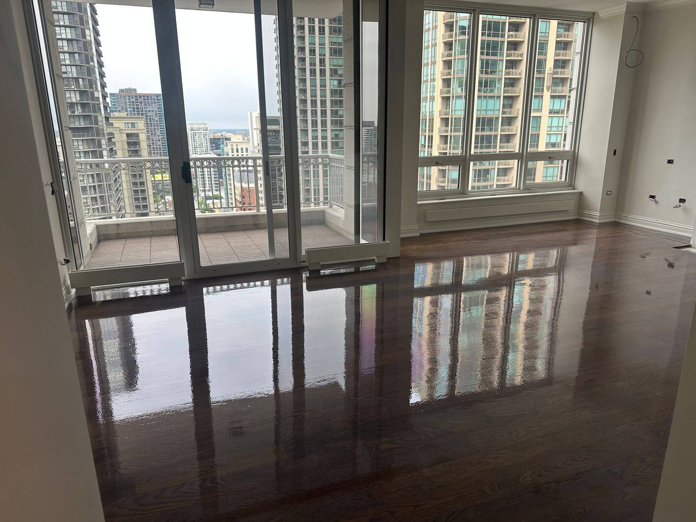 Newly coated engineered white oak floor with the finish still wet and reflecting the Downtown Chicago windows.