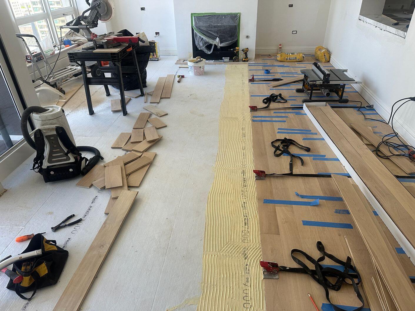 Engineered white oak being fully glued down over the acoustic membrane with flooring straps holding the boards tight.