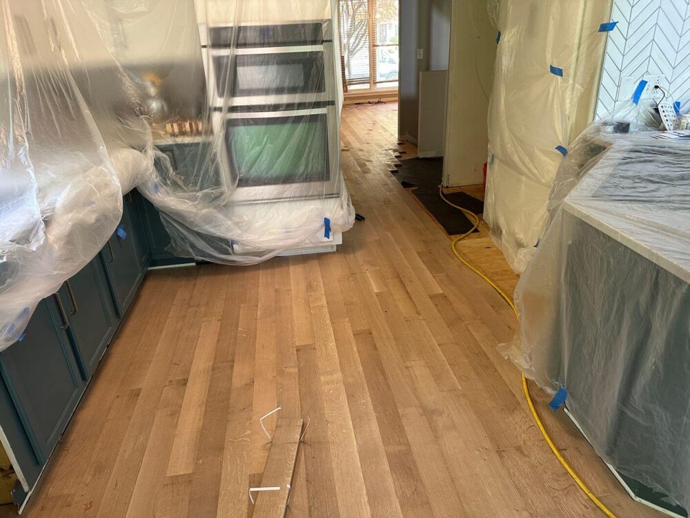 New white oak flooring installed through the kitchen while cabinetry and appliances are protected during the work.
