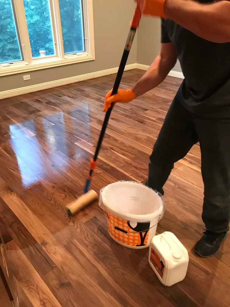 A man applying a glossy finish to hardwood floors with a roller
