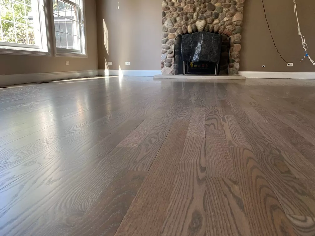 Refinished hardwood flooring with a stone fireplace in a sunlit room