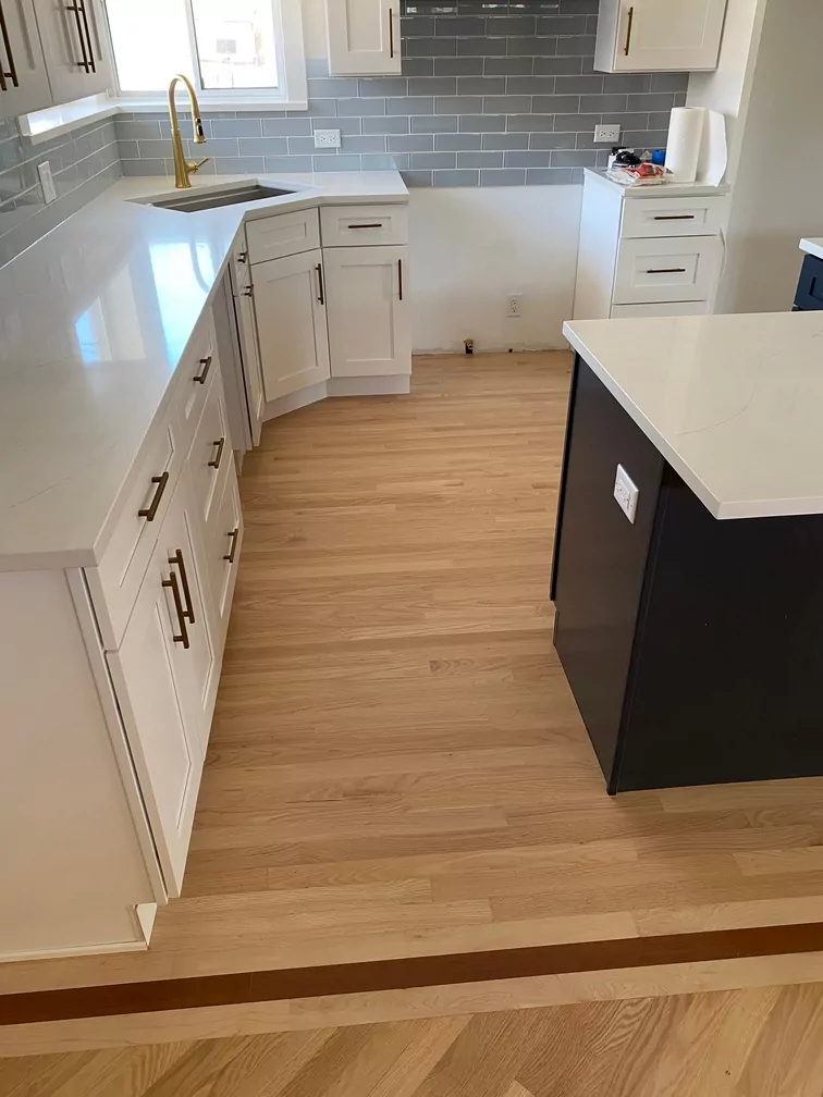 Modern kitchen with light hardwood floors, white cabinets, gray backsplash, and gold fixtures