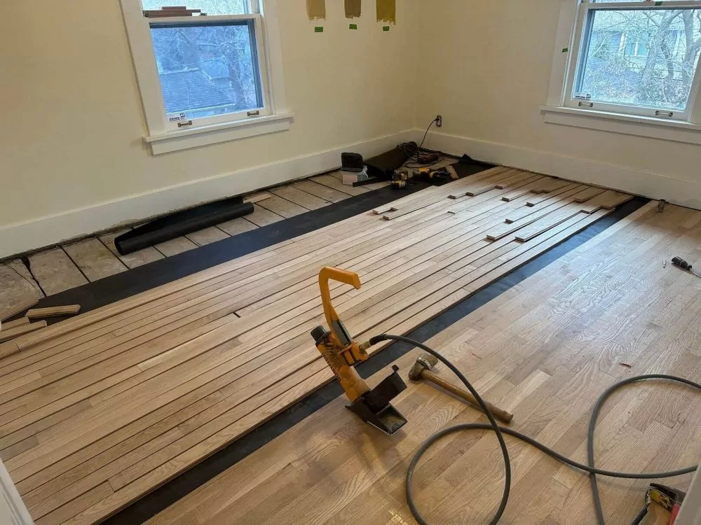 Hardwood floor installation in progress with nail-down boards and tools.