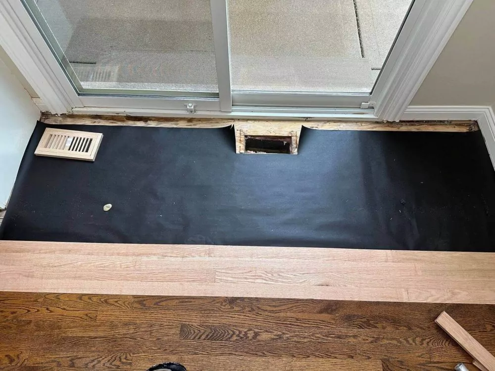 Moisture barrier and underlayment prep near a sliding door before flooring install.