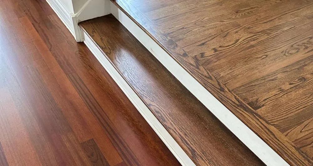 Stair transition from darker oak on the landing to reddish maple below, with the contrast in grain and color making the difference between the two wood species easy to see